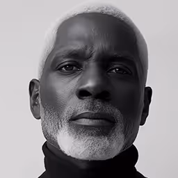 Portrait of an elderly bald man with a gray beard and mustache wearing a black shirt.