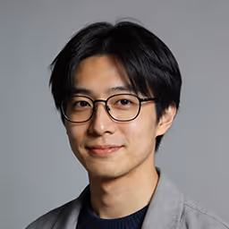 Portrait of a person with short dark hair, black glasses, and wearing a black jacket and white shirt.